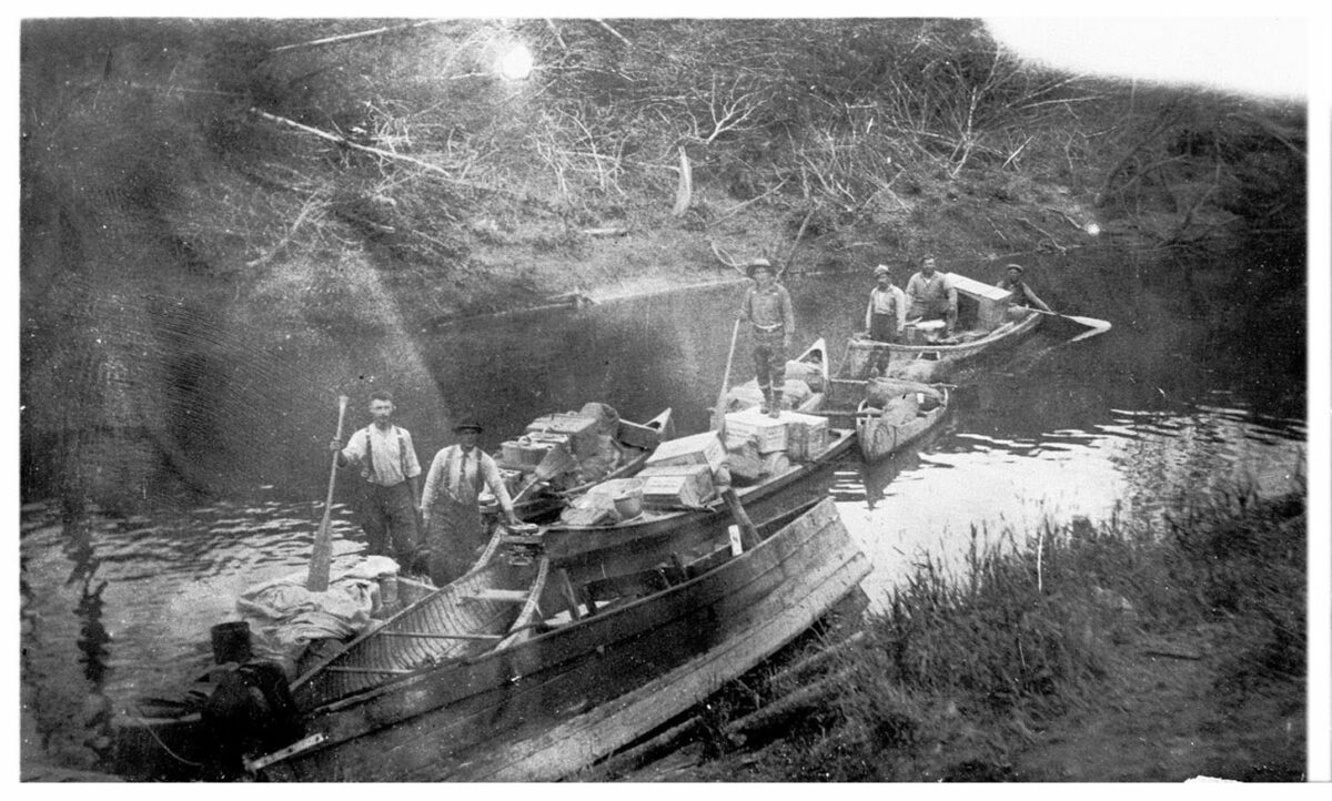 Groupe d’hommes transportant des marchandises sur le Ruisseau Dallaire jusqu’au débarcadère du lac Rouyn, au début de la ville de Rouyn. Vers 1920.